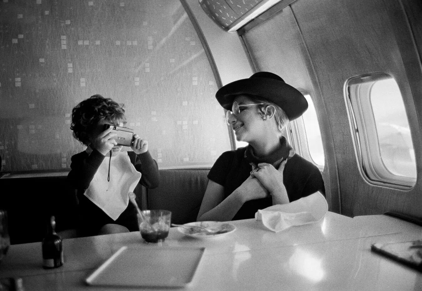 Barbra Streisand smiling at her son Jason Gould aboard a plane en route to London, photographed by Lawrence Schiller, 1969