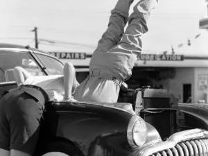 Head over heels car repair photo showing mechanics working upside down on a car engine in San Diego, 1956