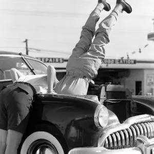 Head over heels car repair photo showing mechanics working upside down on a car engine in San Diego, 1956