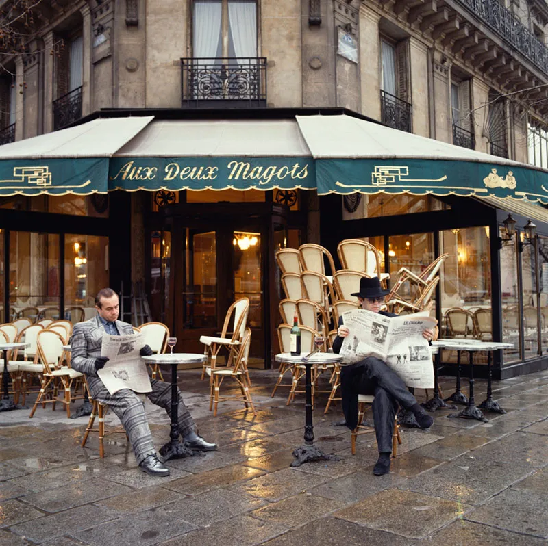 Elton John reading Le Figaro with Bernie Taupin at Aux Deux Magots in Paris