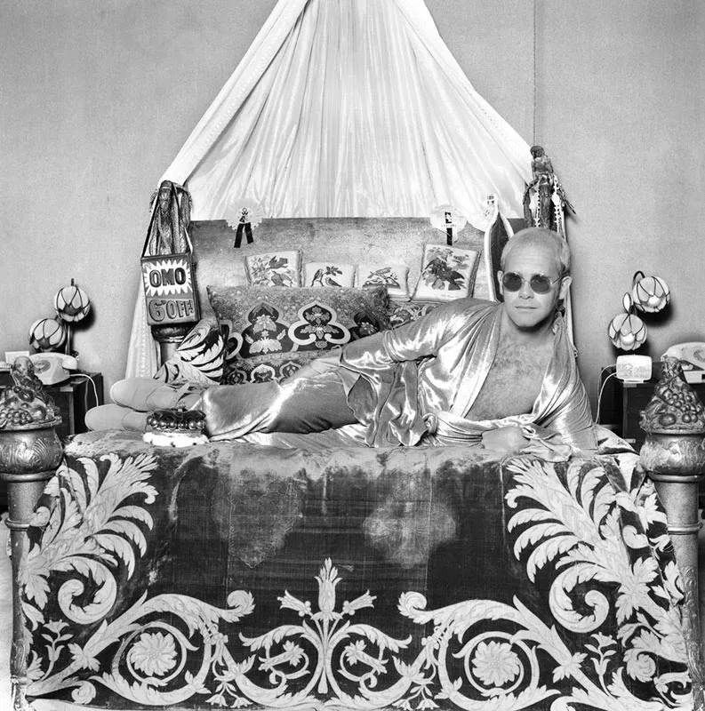 Elton John lying on a lavish bed at his Windsor home in the 1970s, photographed by Terry O’Neill