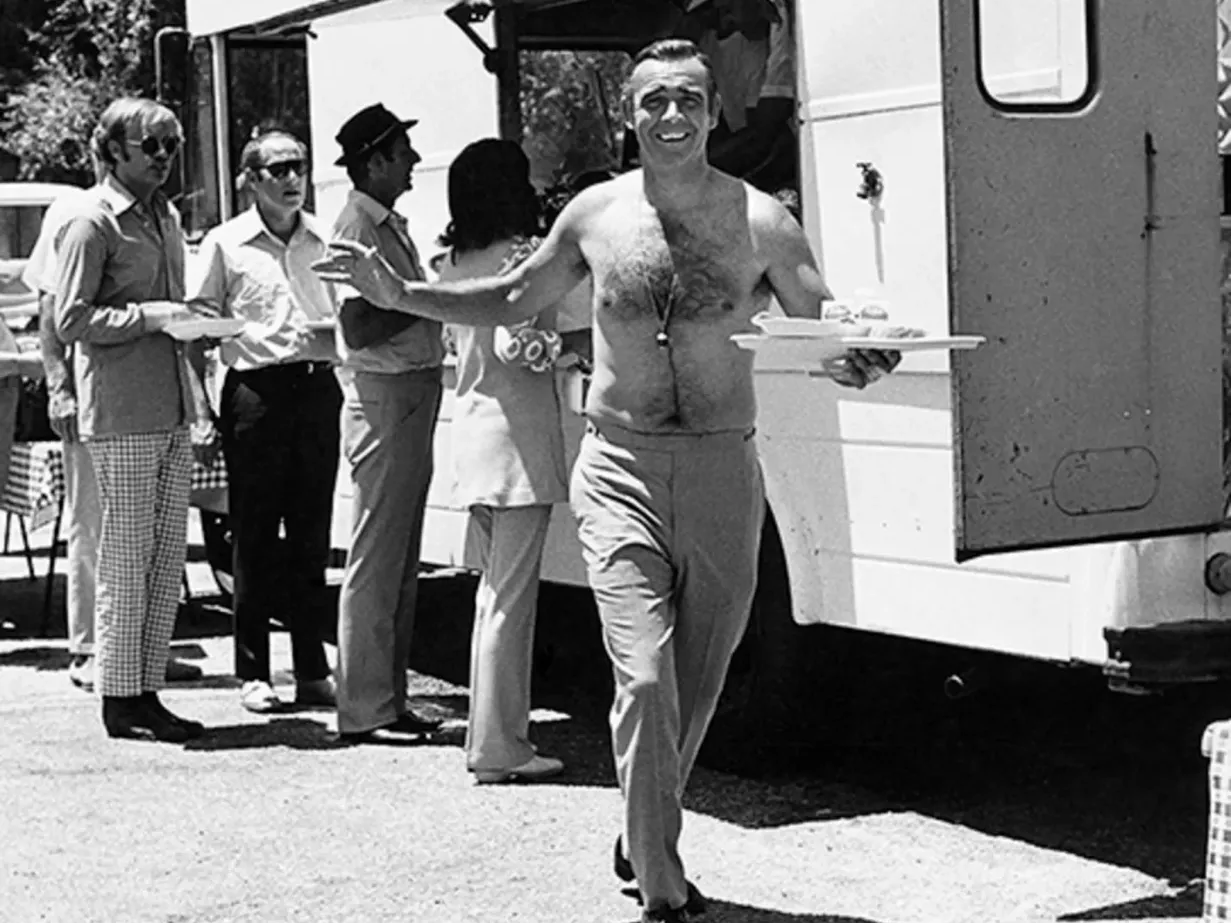 Sean Connery shirtless on the set of Goldfinger, carrying food from a catering truck, photographed by Terry O’Neill, 1964