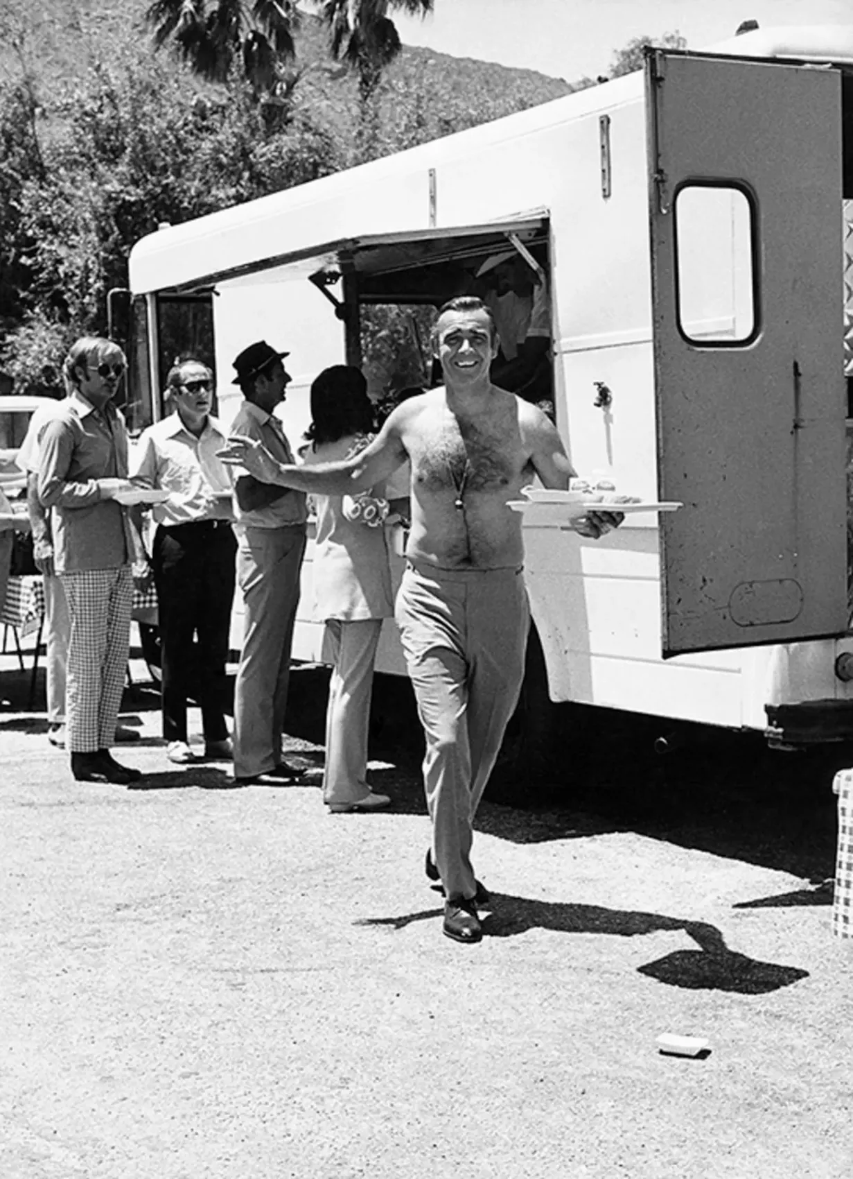 Sean Connery shirtless on the set of Goldfinger, carrying food from a catering truck, photographed by Terry O’Neill, 1964