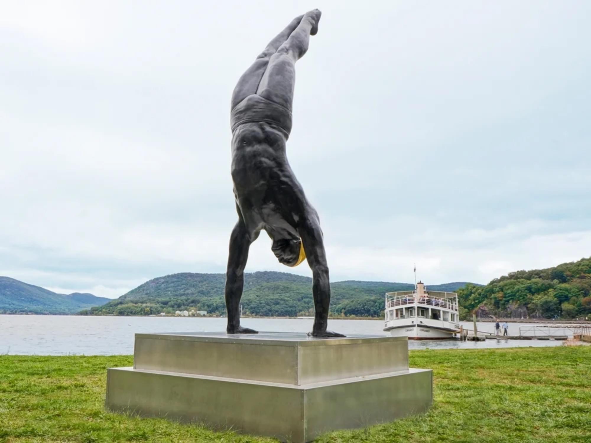 A large outdoor sculpture showing a man standing on his hand by artist Carole Feuerman.